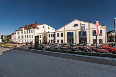 Vor dem Gebäude der Emil Frey Classics AG in Safenwil (5745, Kanton Aargau) sind zahlreiche Oldtimer aufgereiht, während die Sonne die Fassade beleuchtet.