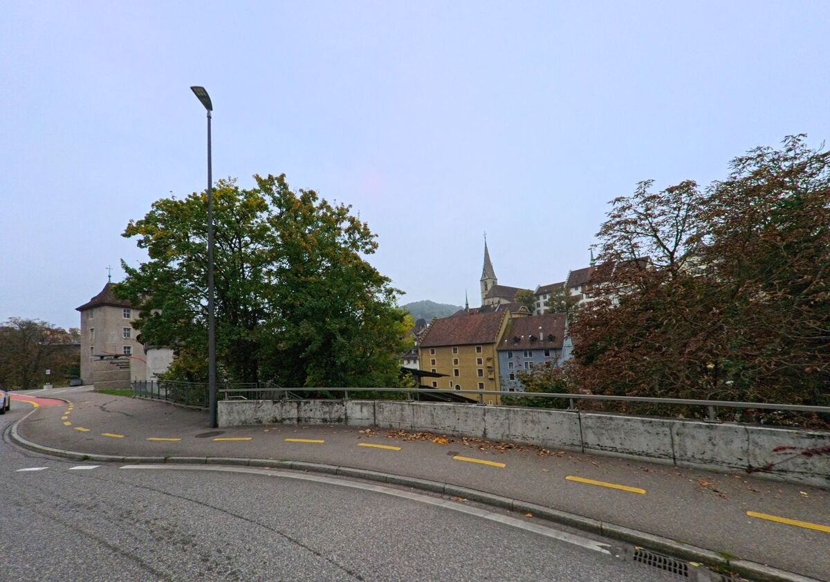 Von einer leicht ansteigenden Strasse in Ennetbaden (5408, Kanton Aargau) aus bietet sich ein Blick auf die Altstadt von Baden mit dem markanten Kirchturm und historischen Gebäuden.