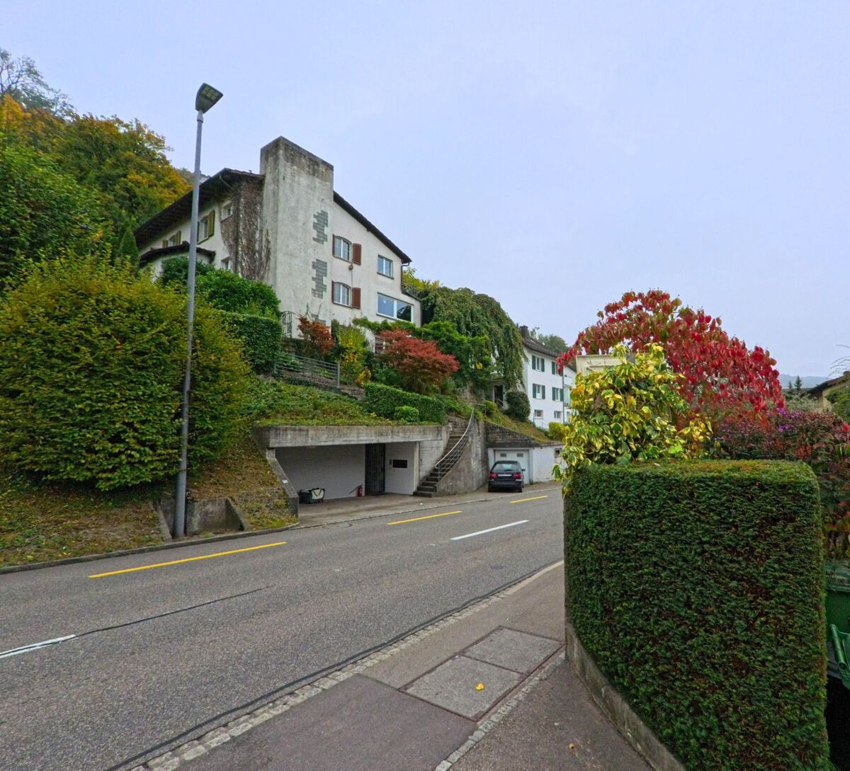 Ein Wohnhaus mit Garten und herbstlich gefärbter Bepflanzung liegt am Hang einer Strasse in Ennetbaden (5408, Kanton Aargau).