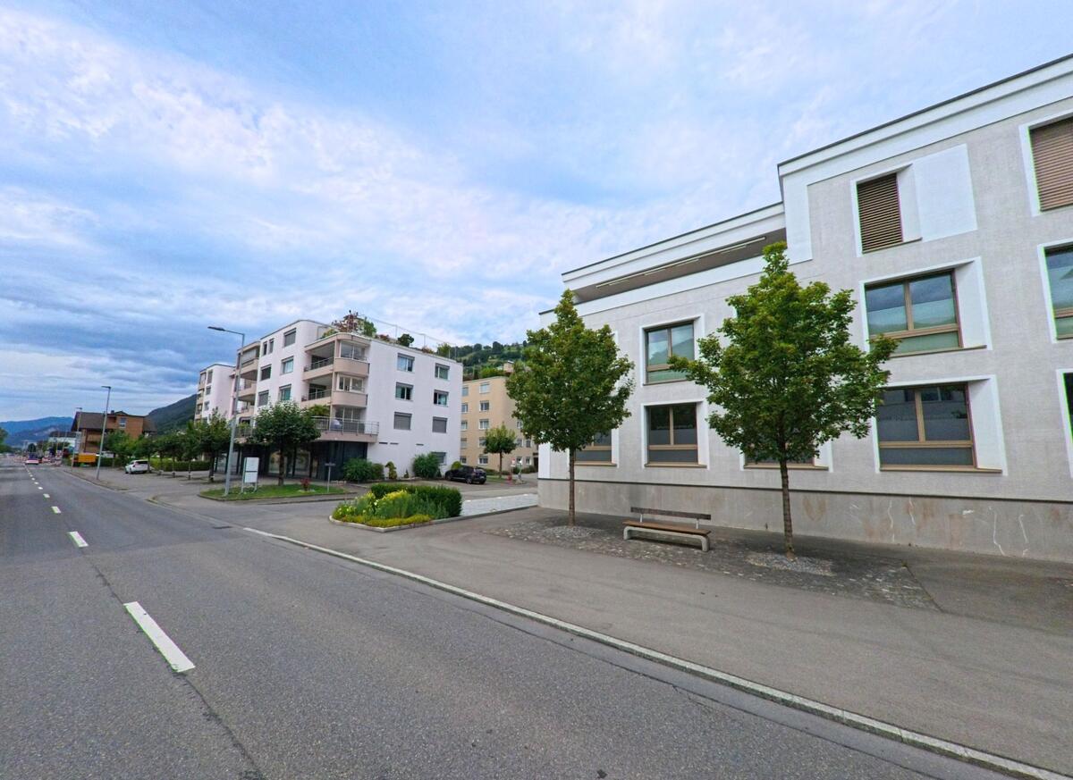 Entlang der Hauptstrasse in Ennetbuergen (6373, Kanton Nidwalden) reihen sich moderne Wohnbauten mit Balkonen und begruenten Bereichen vor bewaldetem Hang.