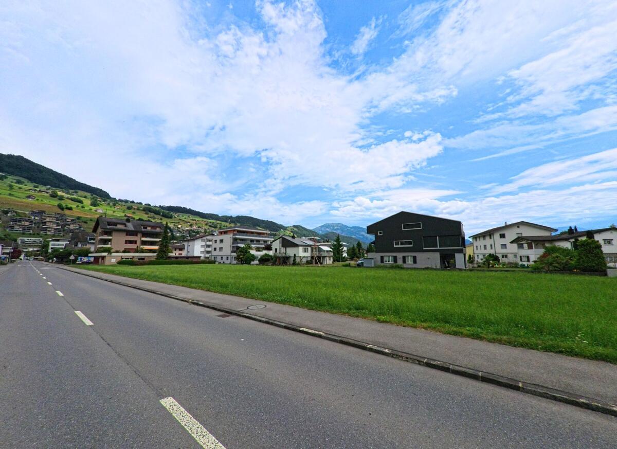 In Ennetbuergen (6373, Kanton Nidwalden) saeumen moderne Wohnhaeuser mit Gartenflaechen eine breite Strasse vor dem Hintergrund terrassierter Hanglagen.