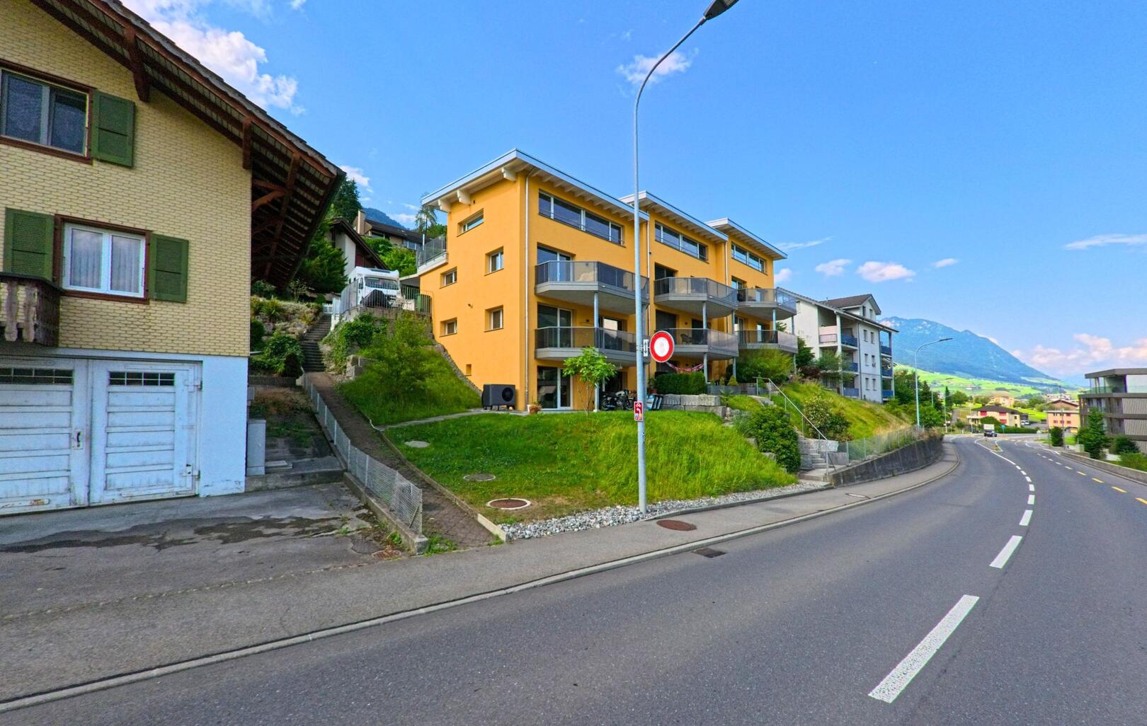 In Ennetmoos (6372, Kanton Nidwalden) verläuft eine kurvige Hauptstrasse entlang moderner Mehrfamilienhaeuser mit Blick auf die umliegenden Berge.