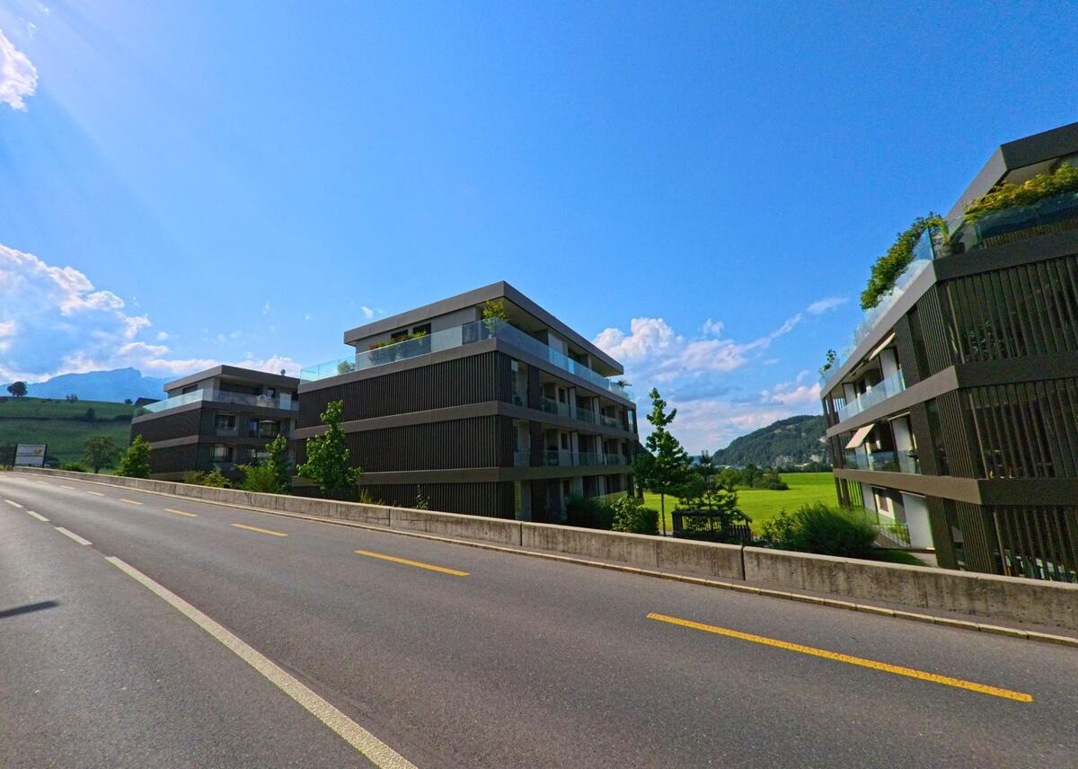 Moderne Wohnbauten in Ennetmoos (6372, Kanton Nidwalden) stehen direkt an einer Hauptstrasse mit Ausblick auf gruenes Kulturland und sanfte Huegel.