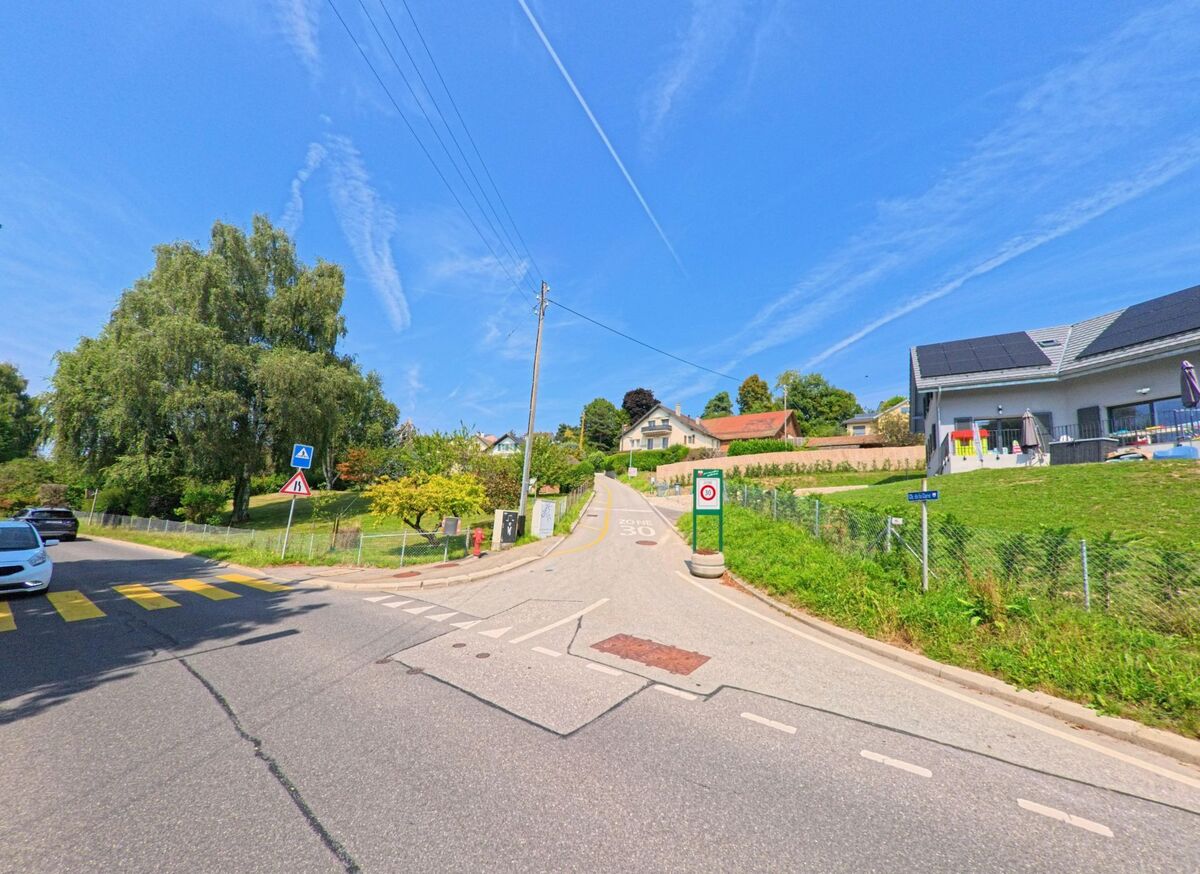 Eine leicht ansteigende Strasse in Épalinges (1066, Kanton Waadt) fuehrt zwischen Wohnhaeusern und Gaerten bergauf, daneben stehen Verkehrsschilder.