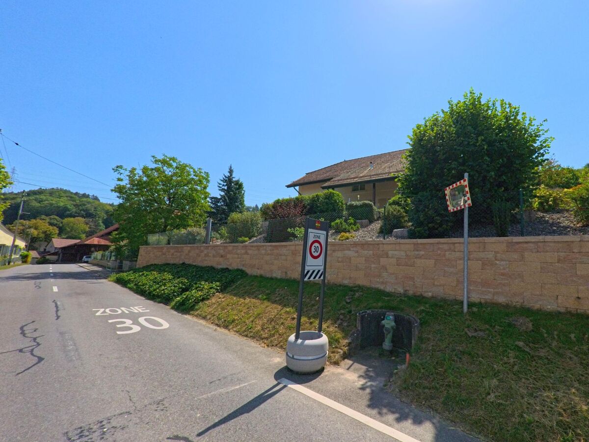 Ein Verkehrsschild markiert die Tempo-30-Zone in Ependes (1434, Kanton Waadt), neben der Strasse liegen Wohnhaeuser und begruente Gaerten.