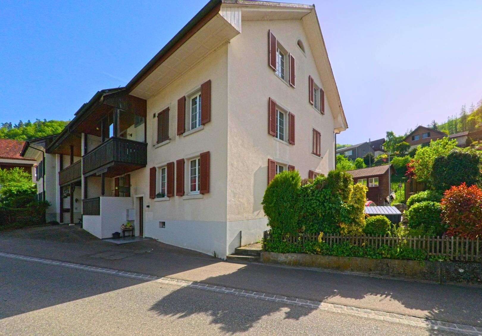 Ein Wohnhaus mit braunen Fensterlaeden steht in Eptingen (4458, Kanton Baselland) an einer ruhig gelegenen Strasse, umgeben von bepflanzten Gaerten am Hang.