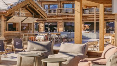 Die Sonnenterrasse des Eringer Hotel in Hérémence (1987, Kanton Wallis) bietet gemütliche Sitzgelegenheiten aus Holz und Stoff mit Blick auf die verschneiten Berge.