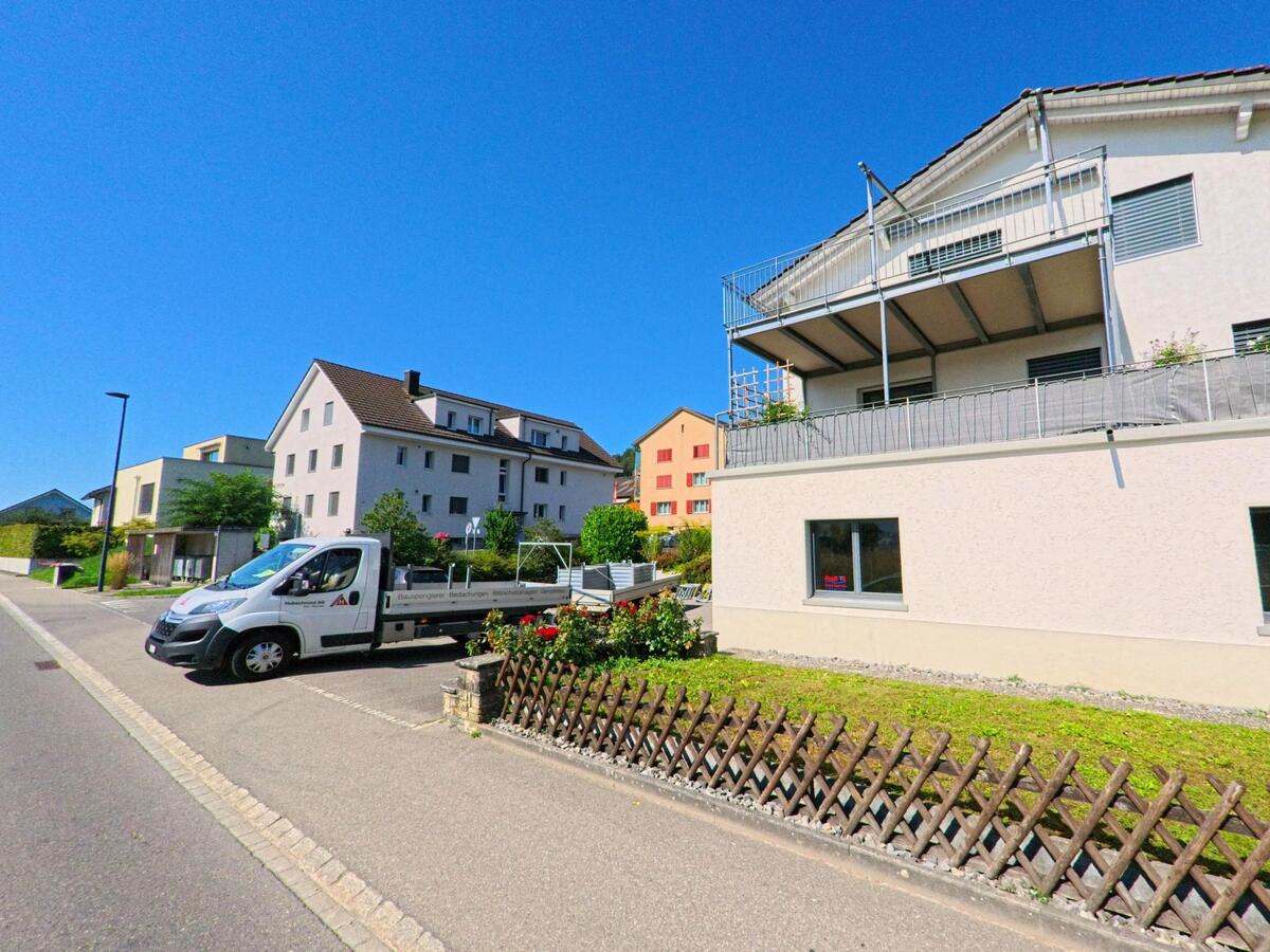 In einer Wohnsiedlung in Erlach (3235, Kanton Bern) stehen mehrgeschossige Haeuser entlang einer ruhigen Strasse, vor der ein Lieferwagen parkiert ist.