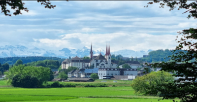 In Muri (5630, Kanton Aargau) erhebt sich das markante Kloster mit seinen roten Tuerme über saftigen Wiesen und Feldern vor der Kulisse der Alpen.