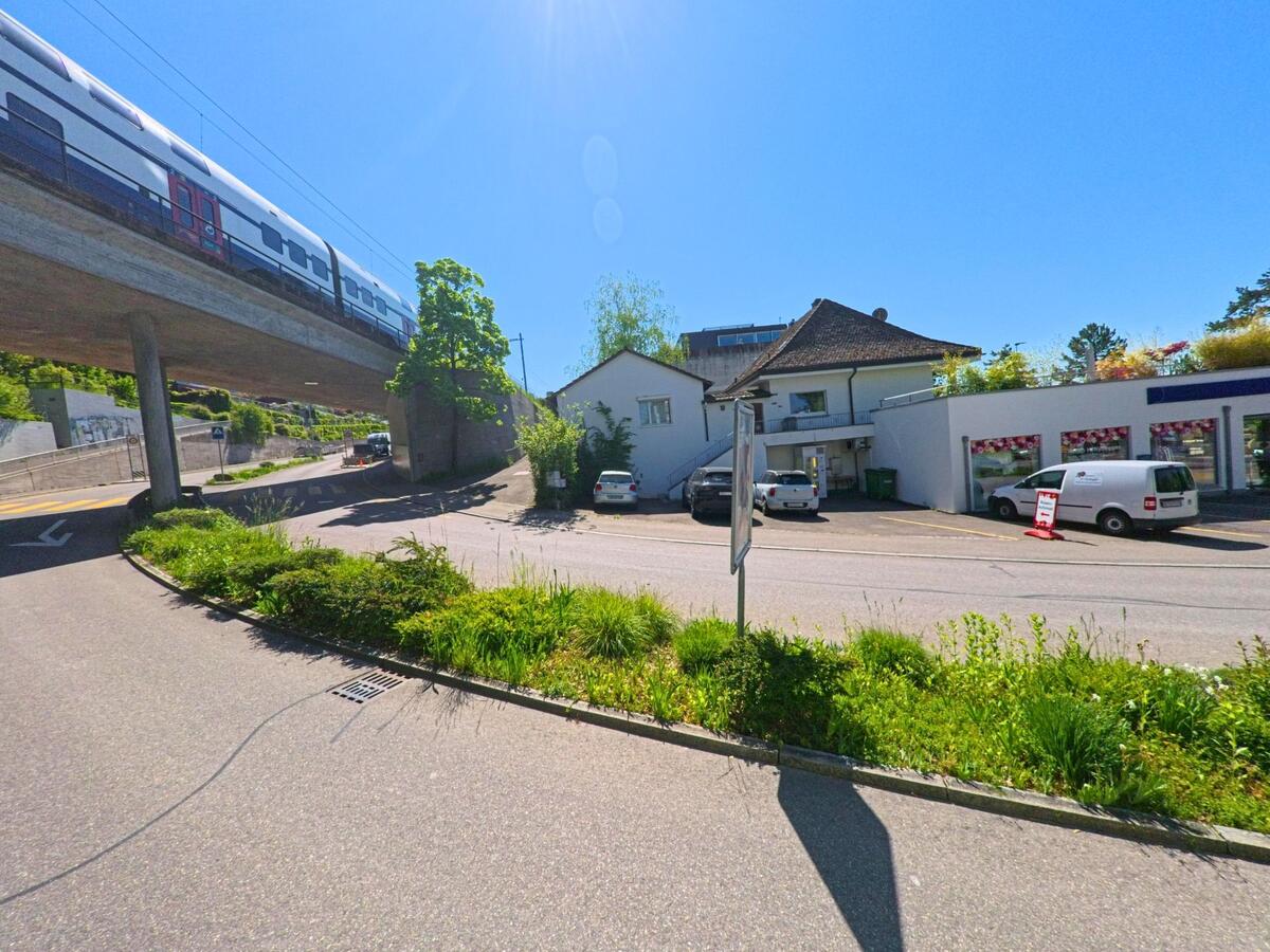 Ein Zug überquert auf einer Betonbrücke das Quartier von Erlenbach im PLZ 8703 im Kanton Zürich, darunter befinden sich Gewerbeflächen und ein Wohnhaus.