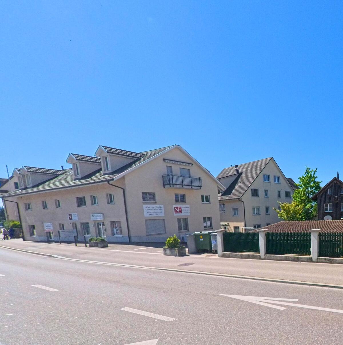 An einer Hauptstrasse in Erlenbach, PLZ 8703 im Kanton Zürich, reihen sich Wohn- und Geschäftsgebäude mit klarer Fassadengestaltung aneinander.