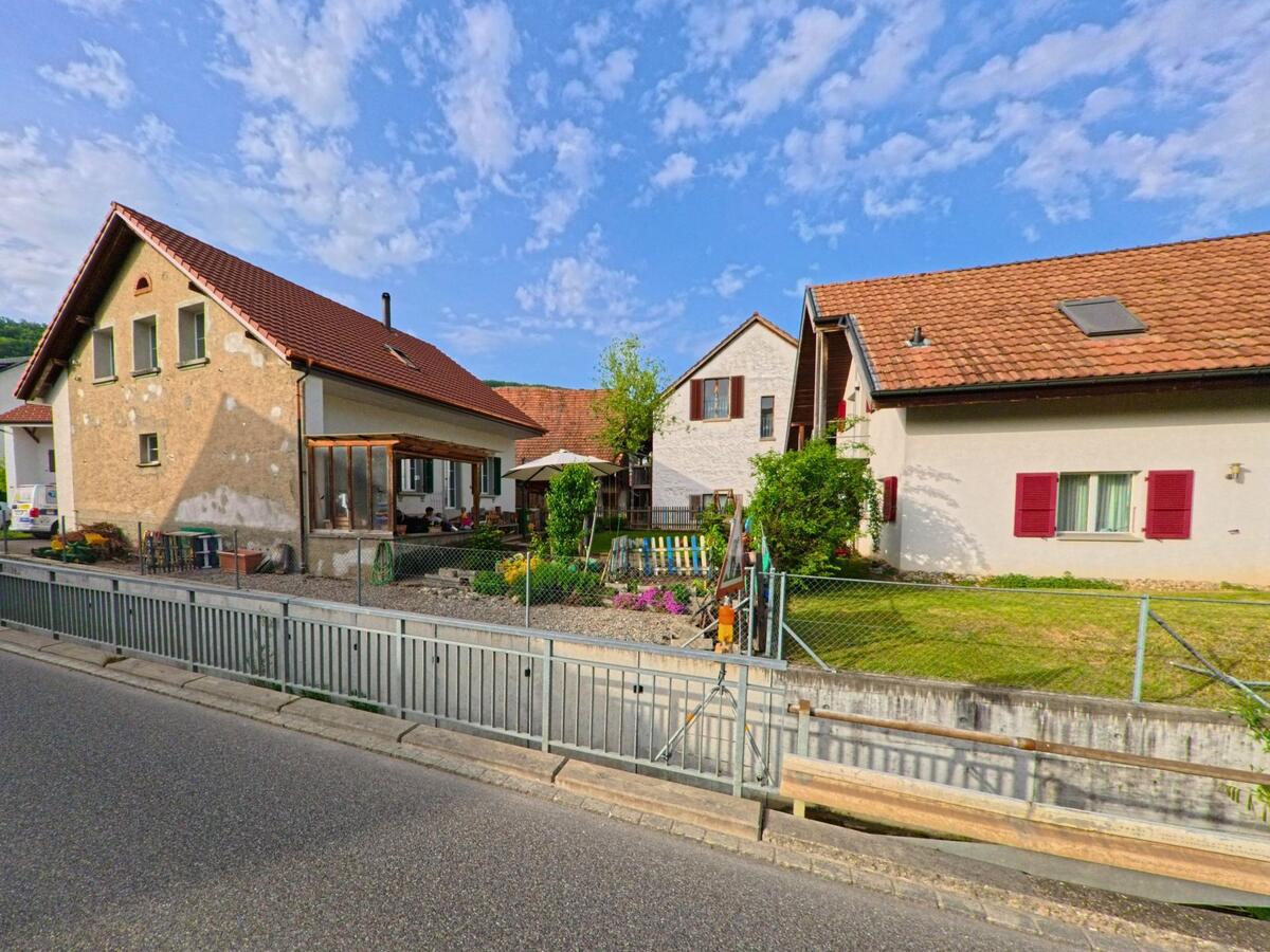 In Erlinsbach (5015, Kanton Solothurn) reihen sich Einfamilienhäuser mit Vorgärten und farbigen Fensterläden entlang einer ruhigen Strasse.