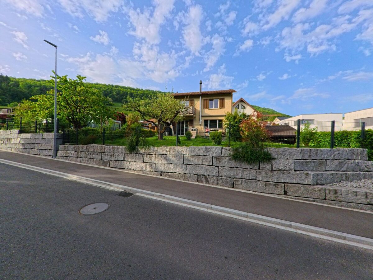 In der Gemeinde Erlinsbach (5017, Kanton Aargau) steht ein Einfamilienhaus mit Garten hinter einer hohen Natursteinmauer an einer ruhigen Quartierstrasse.