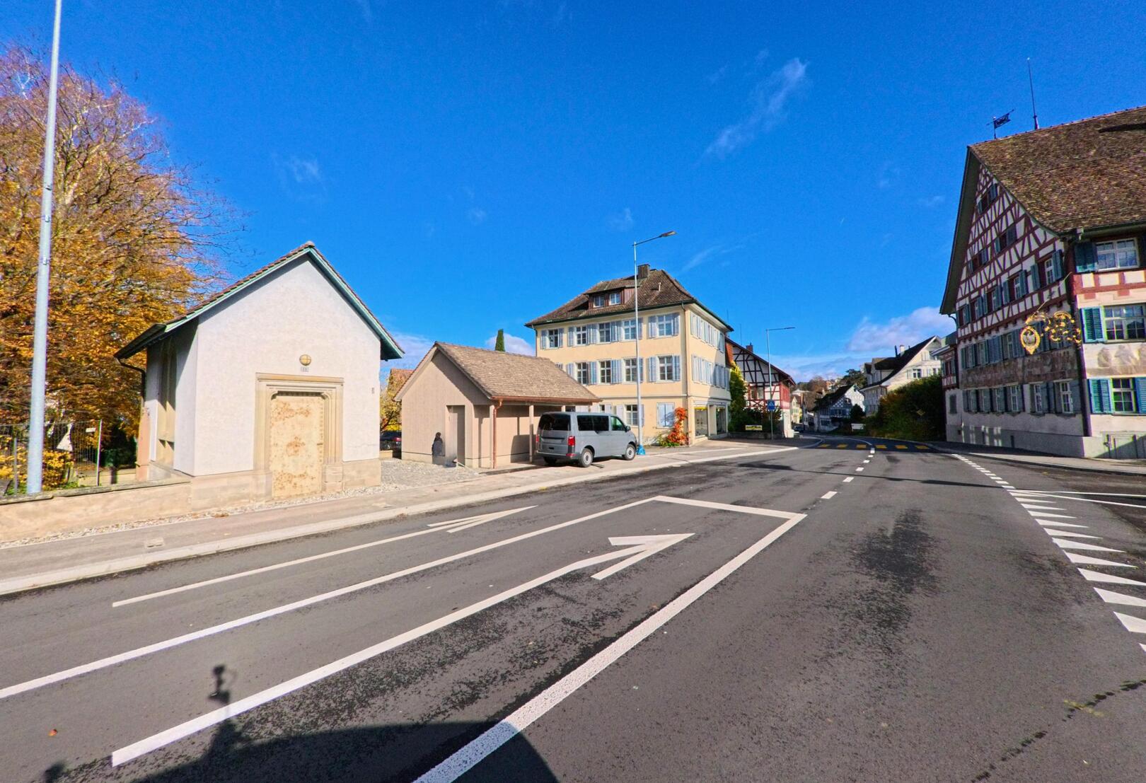 An einer breiten Strassenkreuzung in Ermatingen (8272, Kanton Thurgau) stehen historische Riegelhäuser und moderne Wohnbauten unter blauem Himmel.