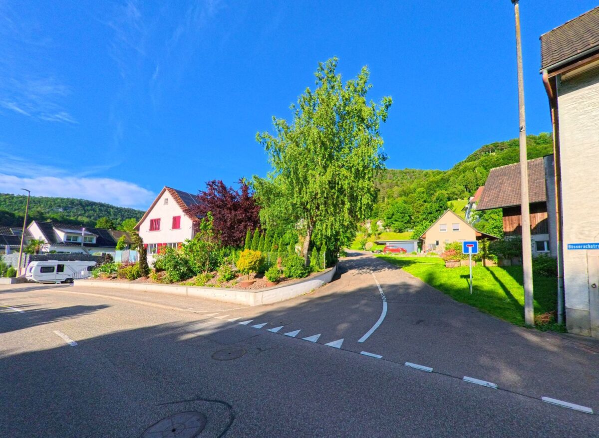  In Erschwil (4228, Kanton Solothurn) zweigt die Büsserachstrasse als Sackgasse von der Hauptstrasse ab und führt an gepflegten Gärten und Einfamilienhäusern vorbei in Richtung der bewaldeten Hänge.