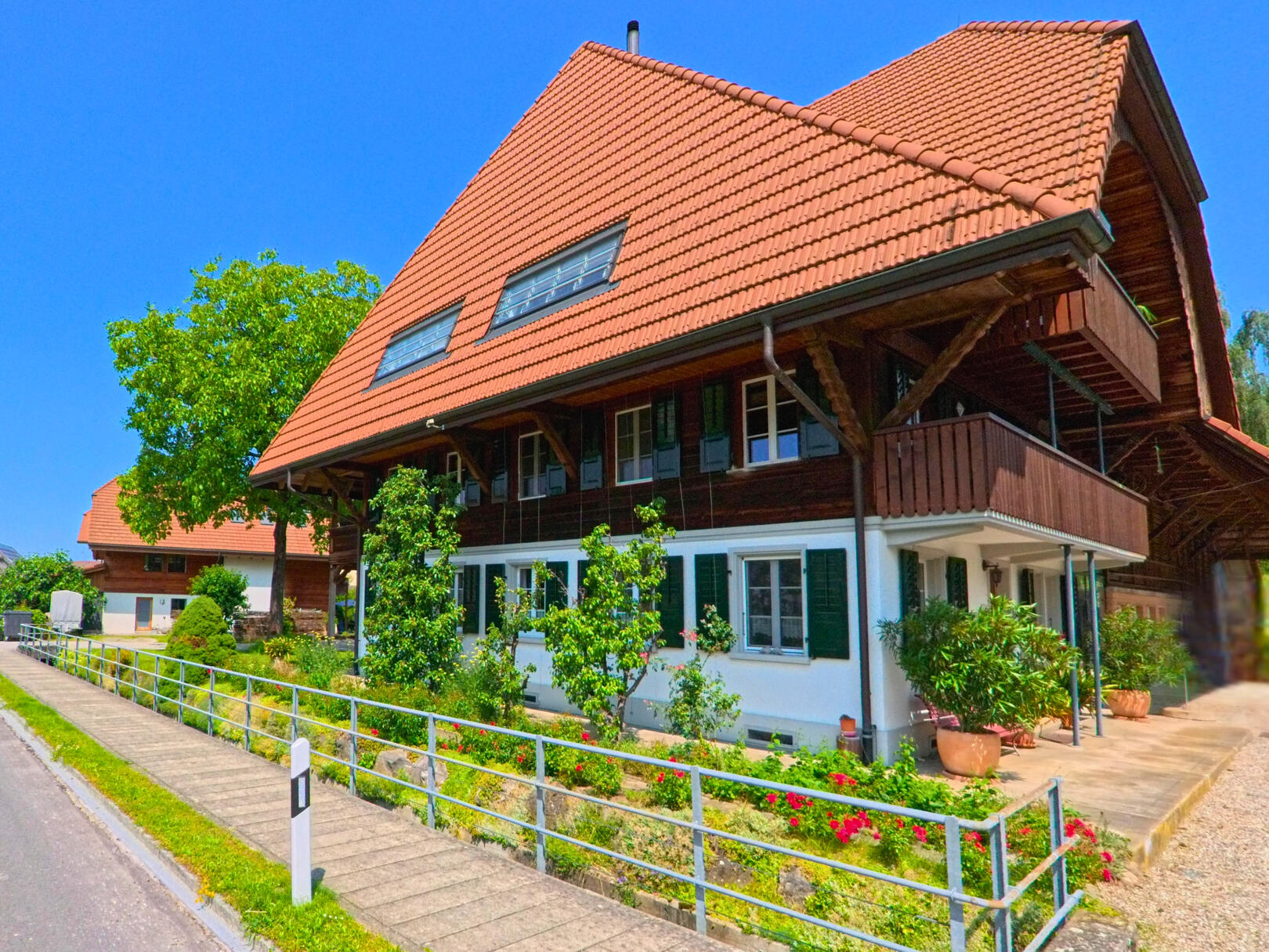In Ersigen (3423, Kanton Bern) steht ein traditionelles Bauernhaus mit grossem Walmdach und gepflegtem Garten an einer ruhigen Strasse.