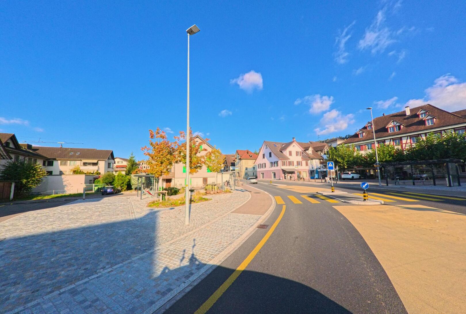 Im Zentrum von Eschenbach (8735, Kanton St. Gallen) laeuft die sanft geschwungene Hauptstrasse an farbigen Hausern, einem Zebrastreifen und einer Bushaltestelle vorbei.