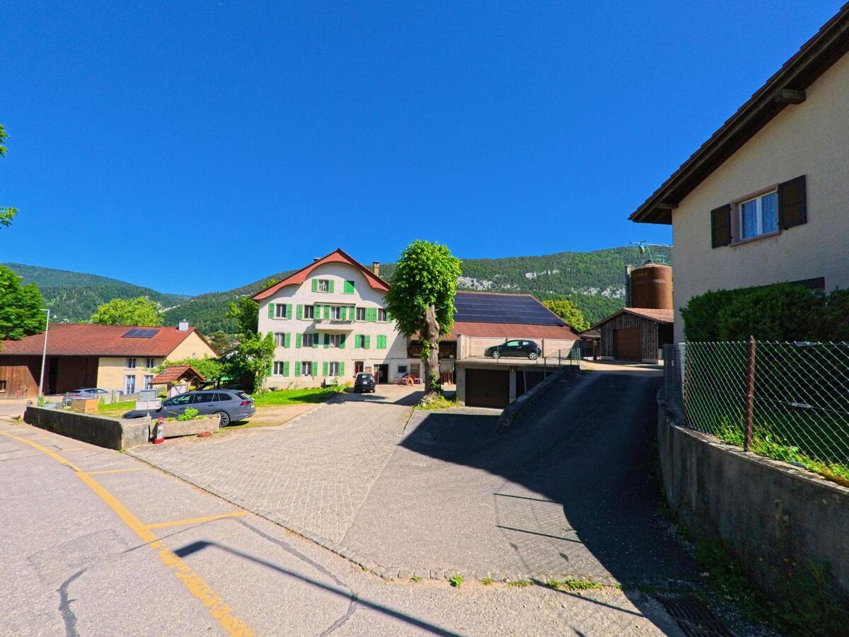 In Eschert (2743, Kanton Bern) steht ein großes, mehrstöckiges Wohnhaus mit grünen Fensterläden im Zentrum eines locker bebauten Quartiers mit Blick auf den Jura.