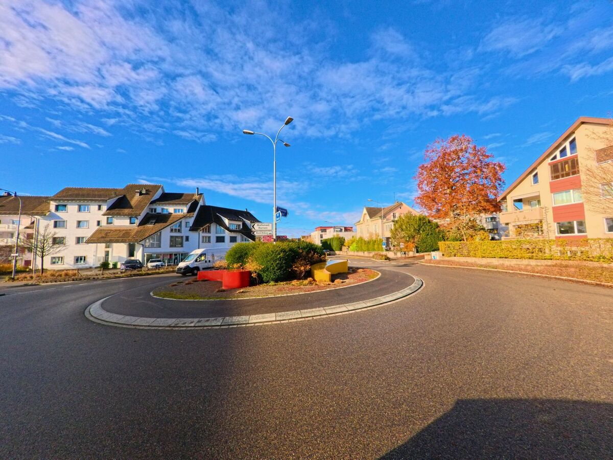 Ein kleiner Kreisel mit bepflanzter Mittelinsel und farbigen Elementen liegt in Eschlikon (8360, Kanton Thurgau) zwischen Wohnhäusern unter klarem Herbsthimmel.
