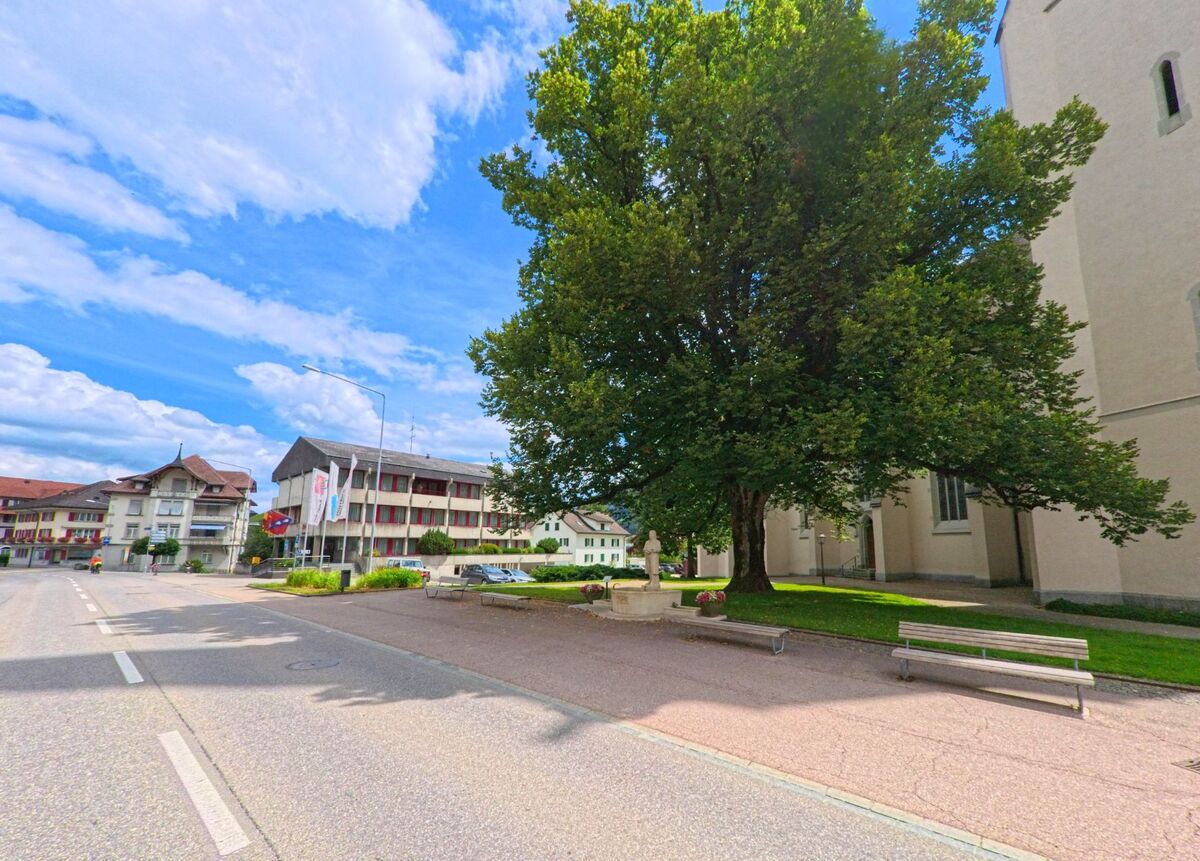 Vor der Kirche in Escholzmatt-Marbach (6182, Kanton Luzern) lädt ein schattiger Platz mit Brunnen und Sitzbänken zum Verweilen ein.