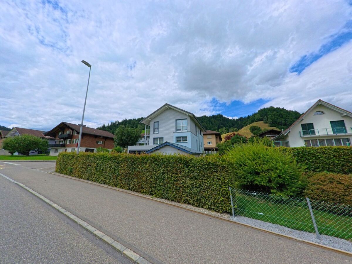 In einem ruhigen Wohnquartier von Escholzmatt-Marbach (6182, Kanton Luzern) reihen sich Einfamilienhäuser entlang einer gepflegten Strasse mit Blick auf bewaldete Hügel.