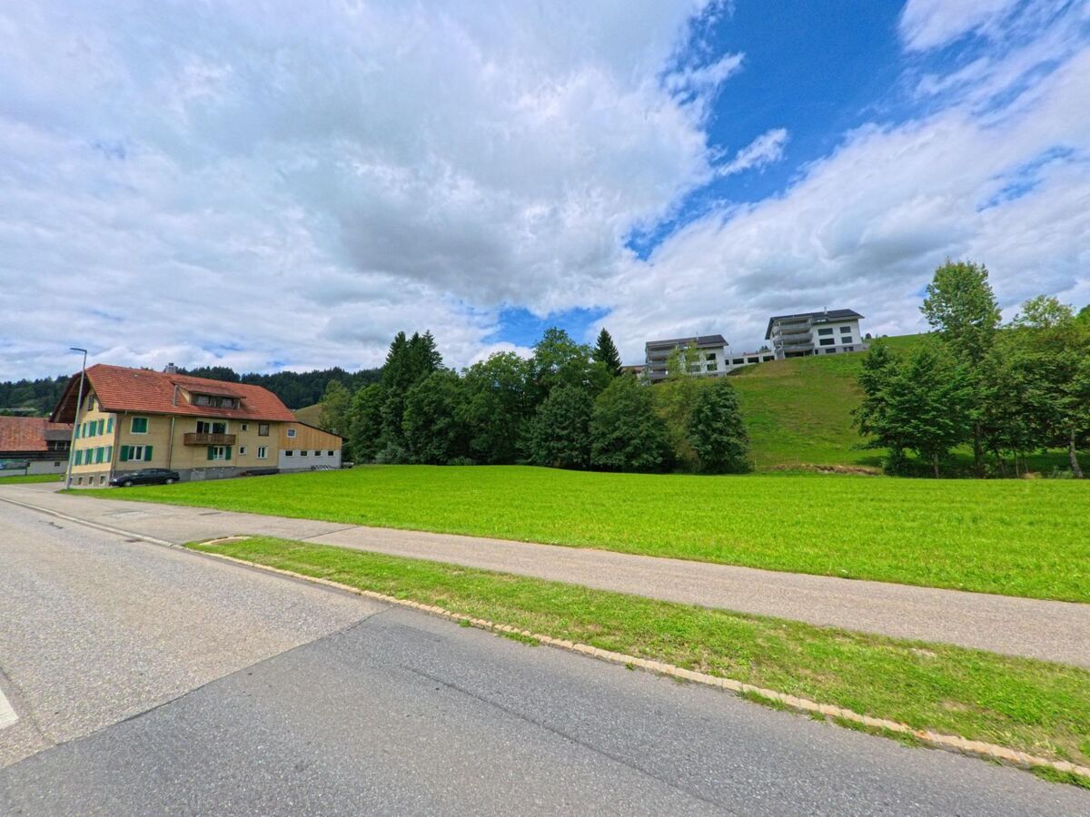  Zwischen traditionellen und modernen Wohnbauten verläuft in Escholzmatt-Marbach (6182, Kanton Luzern) eine Strasse entlang einer gepflegten Grünfläche am Waldrand.