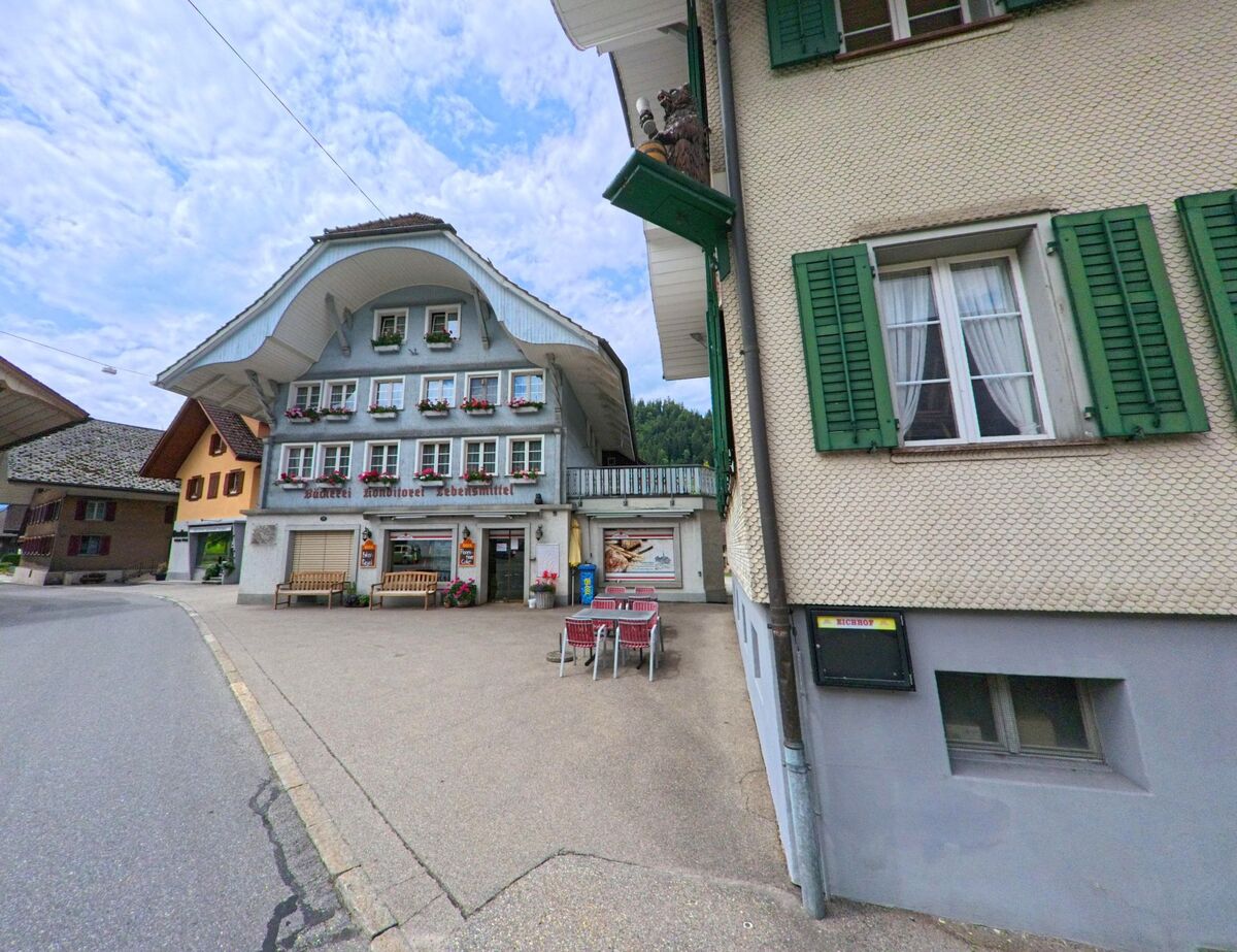 Im Ortskern von Escholzmatt-Marbach (6196, Kanton Luzern) befindet sich eine traditionelle Bäckerei mit auffälligem Dach und blumengeschmückten Fenstern.
