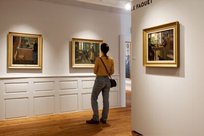 Im Espace Graffenried in Aigle (1860, Kanton Waadt) betrachtet eine Besucherin gerahmte Gemälde in einem hellen Ausstellungsraum.