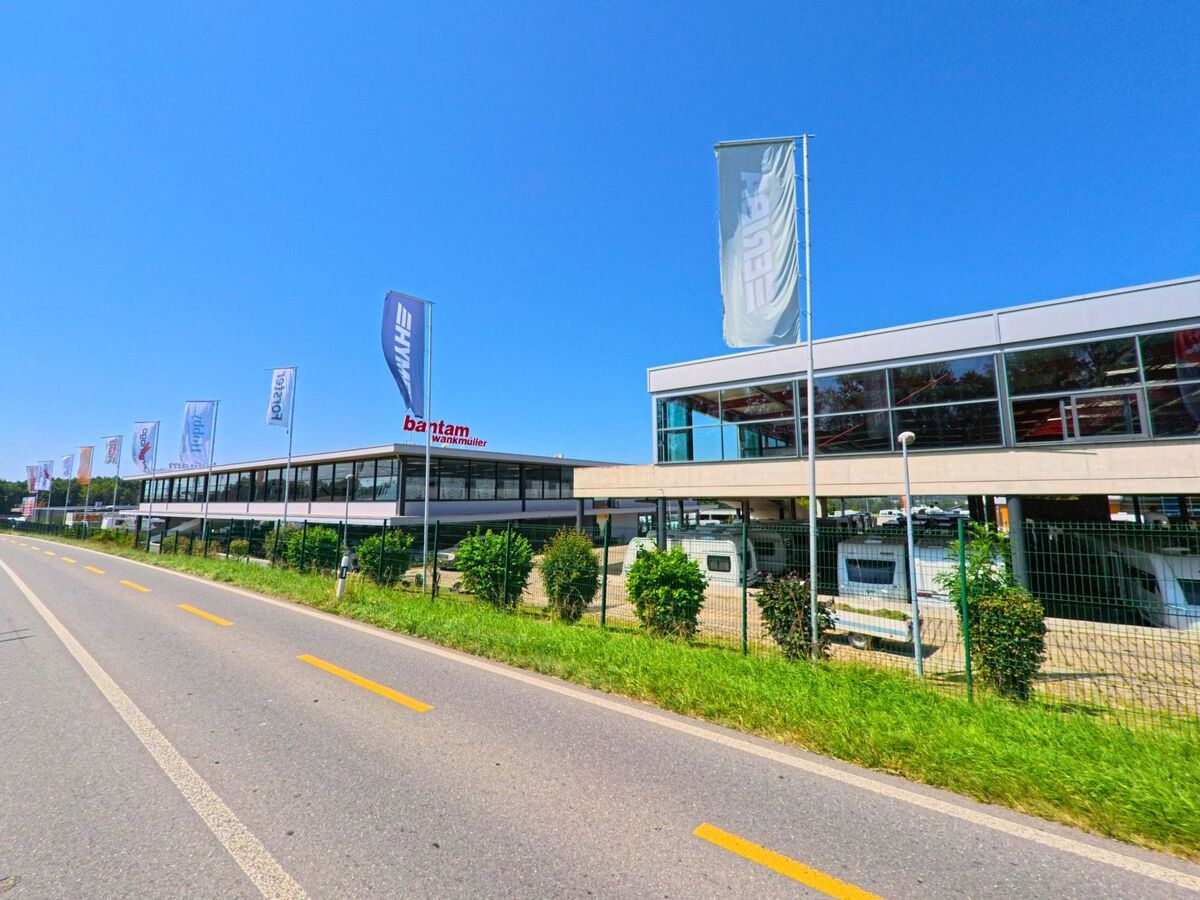 Ein modernes Gebäude in Etagnières (1037, Kanton Waadt) dient als Verkaufsstandort für Wohnwagen, die unter dem Vordach und hinter einem Zaun ausgestellt sind.