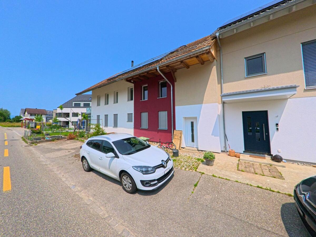  In Etziken (4554, Kanton Solothurn) reihen sich modernisierte Wohnhäuser mit bunten Fassaden an einer Nebenstrasse mit Vorgärten und geparkten Fahrzeugen.