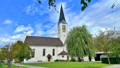 Die evangelisch-reformierte Kirche steht in Diepoldsau (9444) im Kanton St. Gallen mit hohem Turm neben einer grossen Weide auf einer Gruenflaeche.