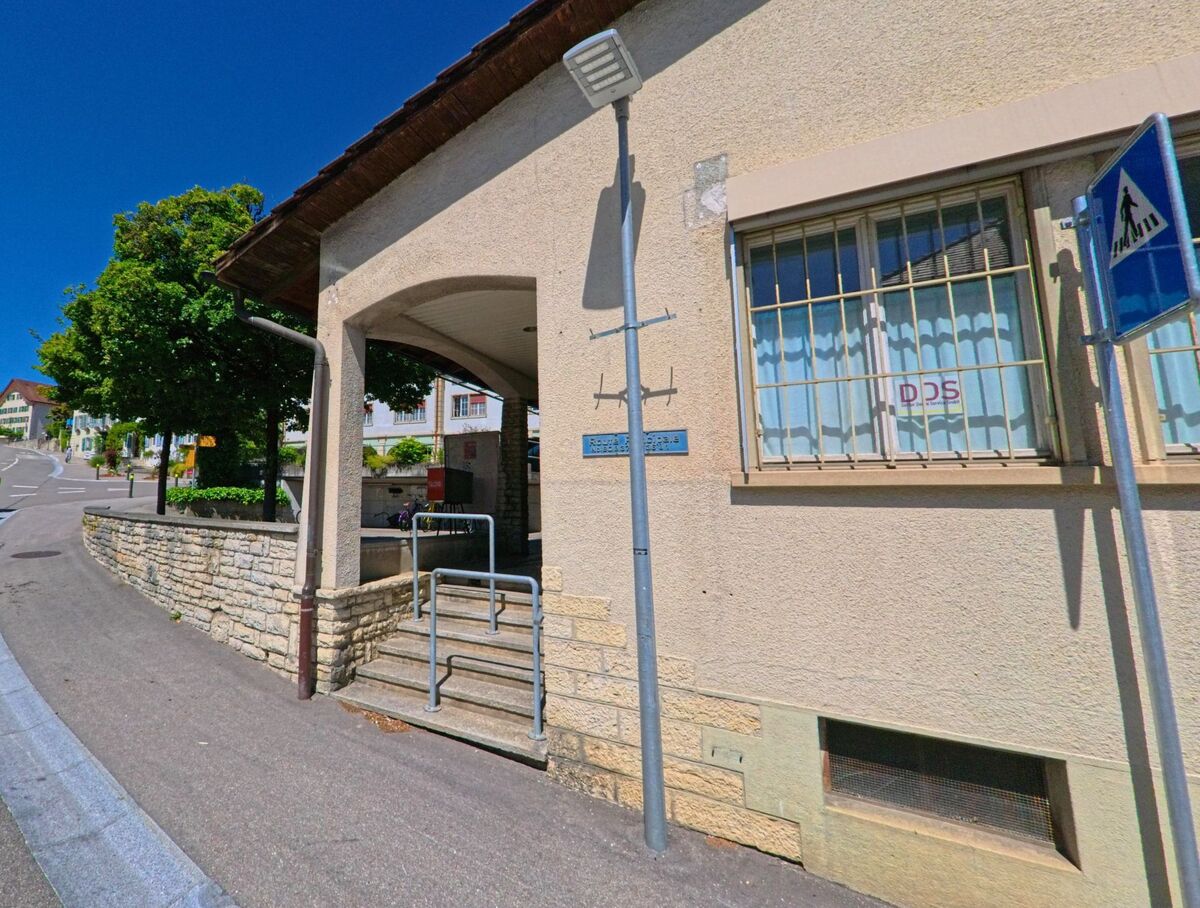 In Evilard (2533, Kanton Bern) liegt ein Gebäude mit überdachtem Eingangsbereich an einer leicht ansteigenden Strasse im Ortszentrum.