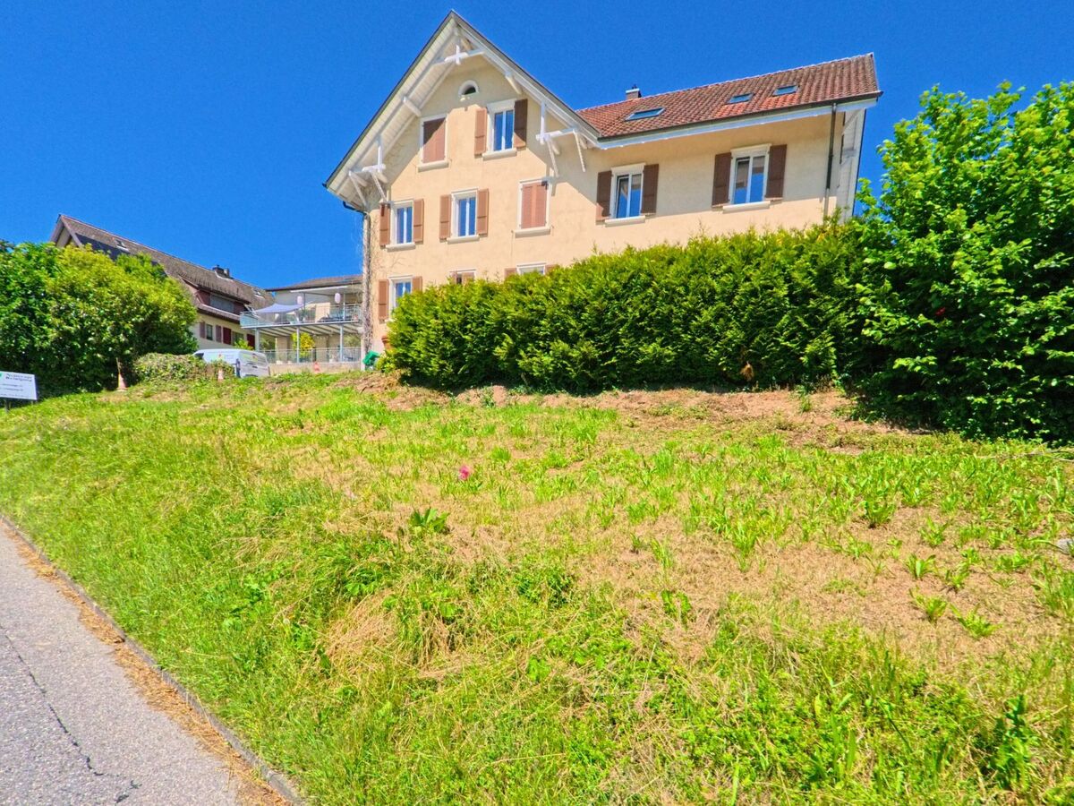 Ein Wohnhaus mit Fensterläden steht in Evilard (2533, Kanton Bern) oberhalb einer gemähten Grünfläche am sonnigen Hang.