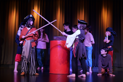 Auf der Bühne des fabriggli werdenberger kleintheater in Buchs (9470, Kanton St. Gallen) probt eine Kindergruppe in Piratenkostümen einen lebhaften Fechtkampf vor einem roten Fass.