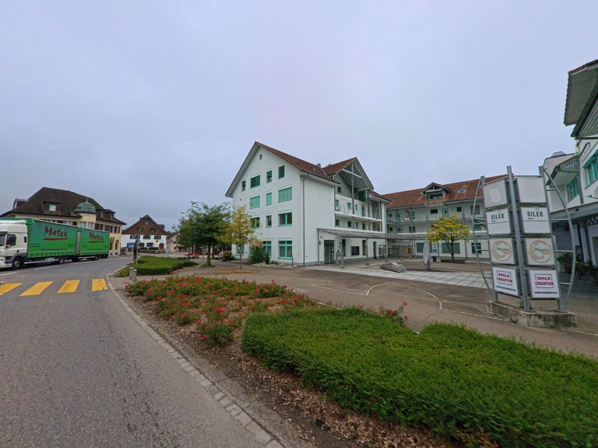 Im Zentrum von Fahrwangen (5615, Kanton Aargau) befindet sich ein moderner Platz mit Geschäfts- und Wohnhäusern, bepflanzten Flächen und einem Zebrastreifen an der Strasse.