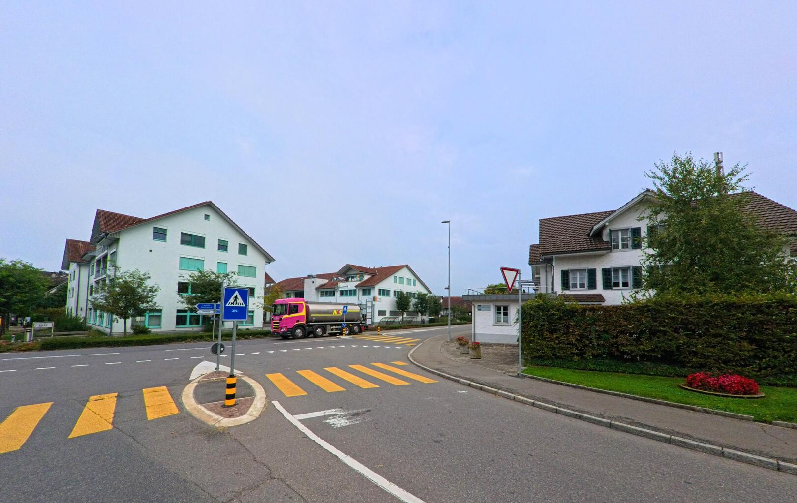 Ein Zebrastreifen mit Verkehrsinsel und einem auffälligen Lastwagen prägt diese Strassenszene im Zentrum von Fahrwangen (5615, Kanton Aargau).