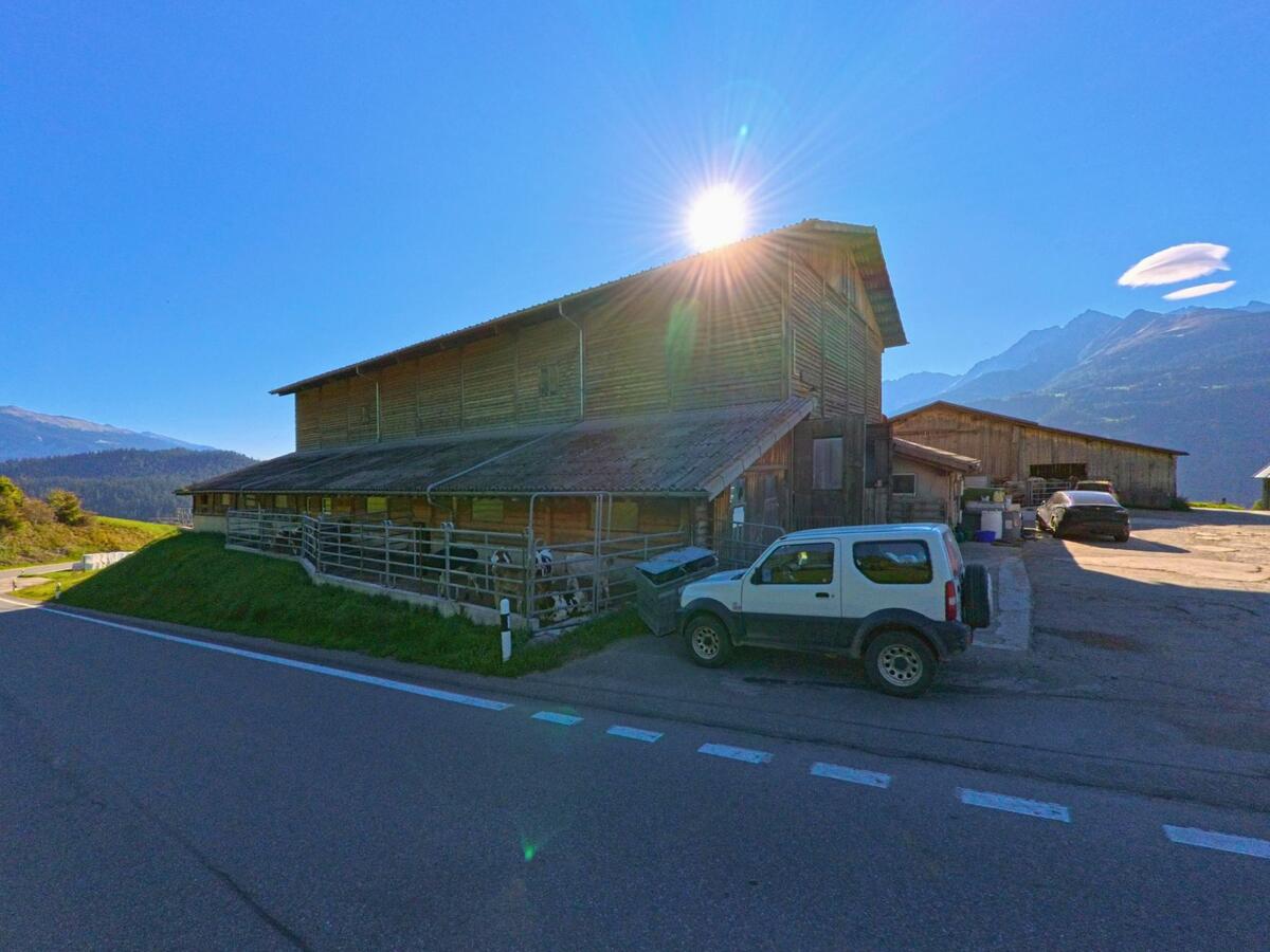 Ein Bauernhof am Ortsrand von Falera (7153, Kanton Graubuenden) liegt in der Sonne, waehrend im Hintergrund die Berge der Surselva zu sehen sind.
