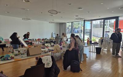 In Brugg (5116, Kanton Aargau) stehen Kinder und Erwachsene in einem hellen Raum zwischen Tischen mit Spielwaren und weiteren Gegenständen.