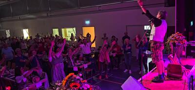 Mitglieder und Gäste des Fanclubs SILVANAS Schweiz aus Niederbuchsiten (4626, Kanton Solothurn) feiern gemeinsam bei einem Konzert in einer Halle und bewegen sich zur Musik vor der Bühne.