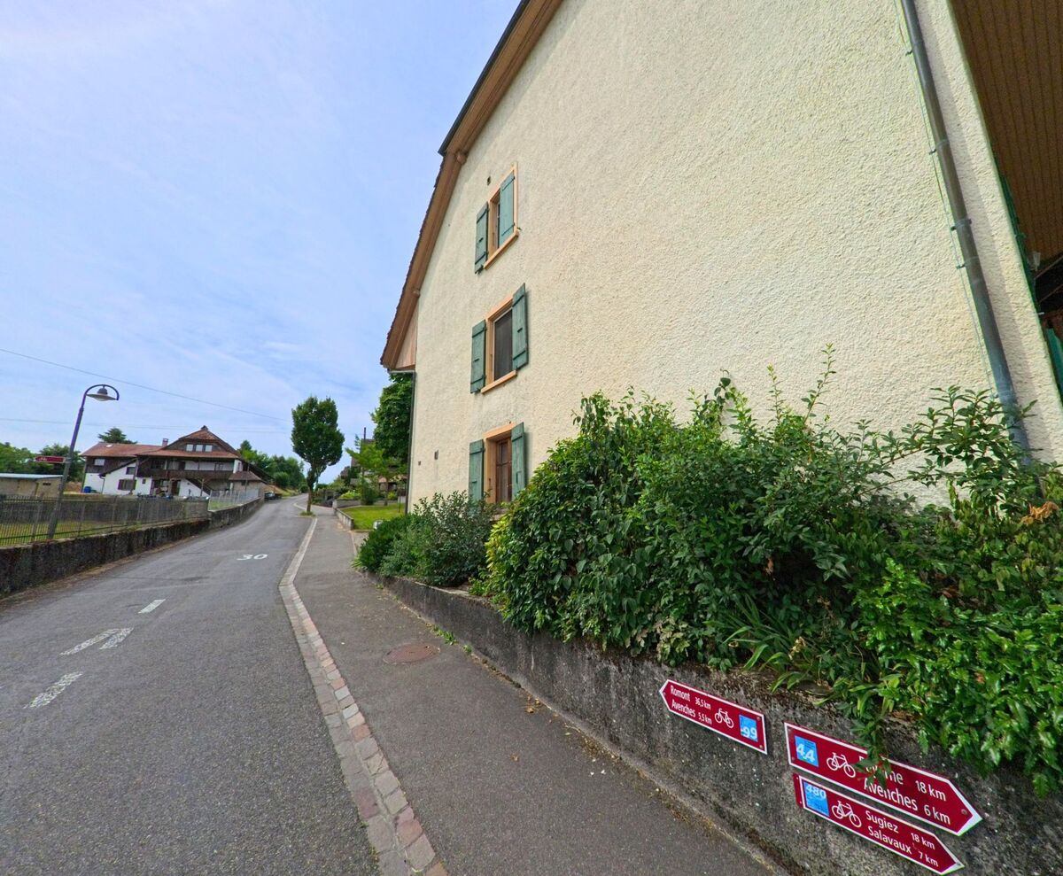 In Faoug (1595, Kanton Freiburg) verläuft eine schmale Strasse durch ein Wohngebiet mit Velowegweisern, die in umliegende Orte wie Avenches und Salavaux führen.