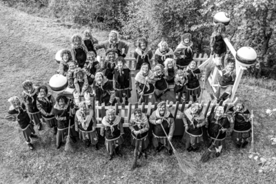 In Feusisberg (8834, Kanton Schwyz) steht die Fasnachtsgesellschaft Schindellegi in traditionellen Hexenkostuemen dicht zusammengruppiert vor einer Kulisse aus Baumen und einem Wagen.