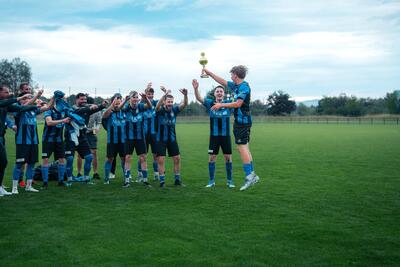 Fussballspieler feiern gemeinsam auf dem Spielfeld und heben einen Pokal in die Hoehe in Heimberg (3627, Kanton Bern) nach einem Sieg.