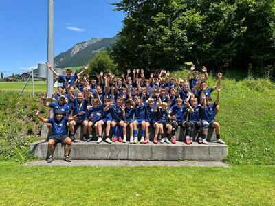 Auf einer Sitzstufe jubelt in Mümliswil (4717, Kanton Solothurn) eine Jugendmannschaft des FC gemeinsam mit Trainerteam nach einem erfolgreichen Anlass im Freien.