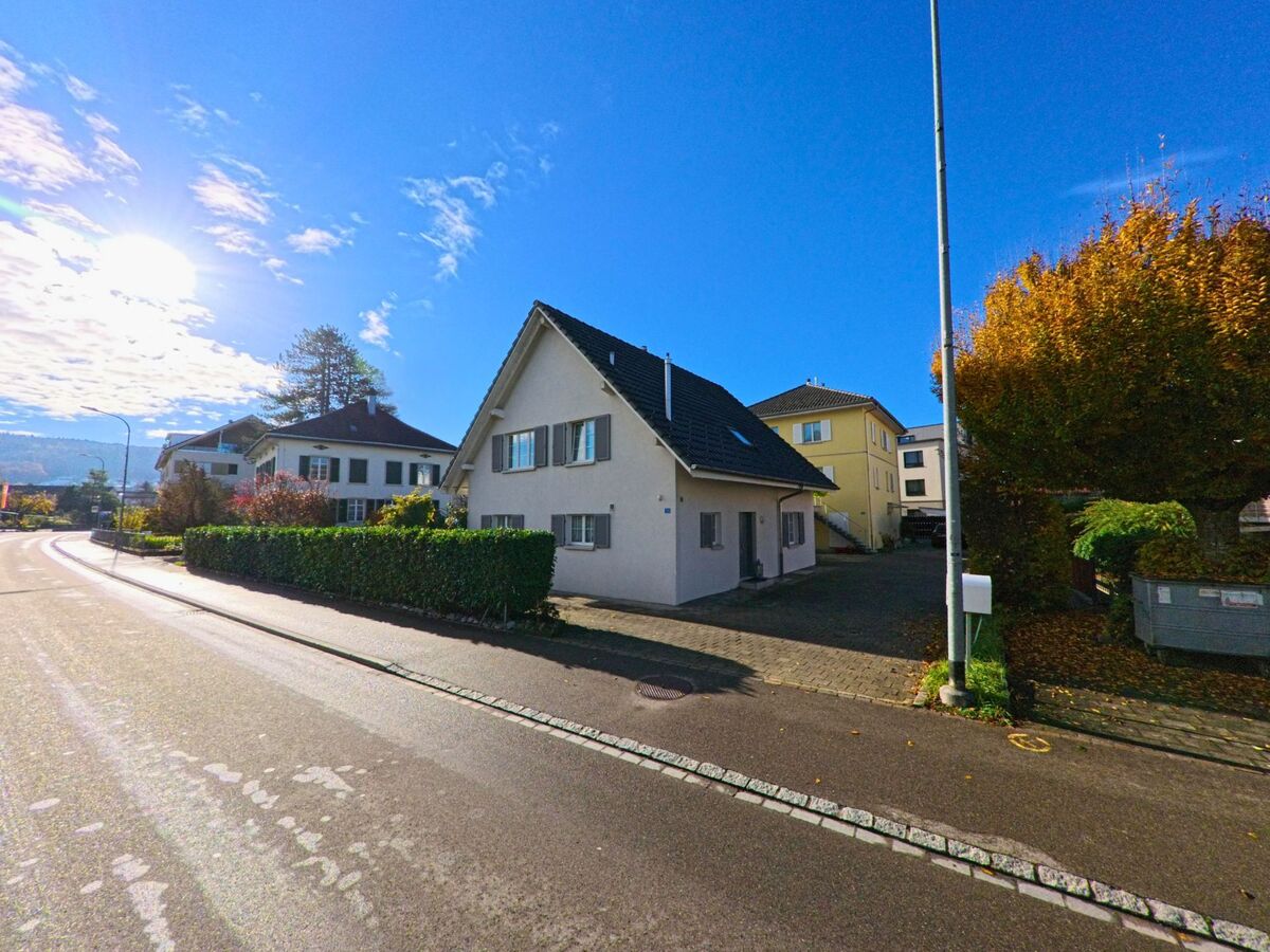 An einer sonnigen Strasse in Felben-Wellhausen (8552, Kanton Thurgau) steht ein Einfamilienhaus mit Hecke und Vorplatz neben herbstlichen Bäumen.