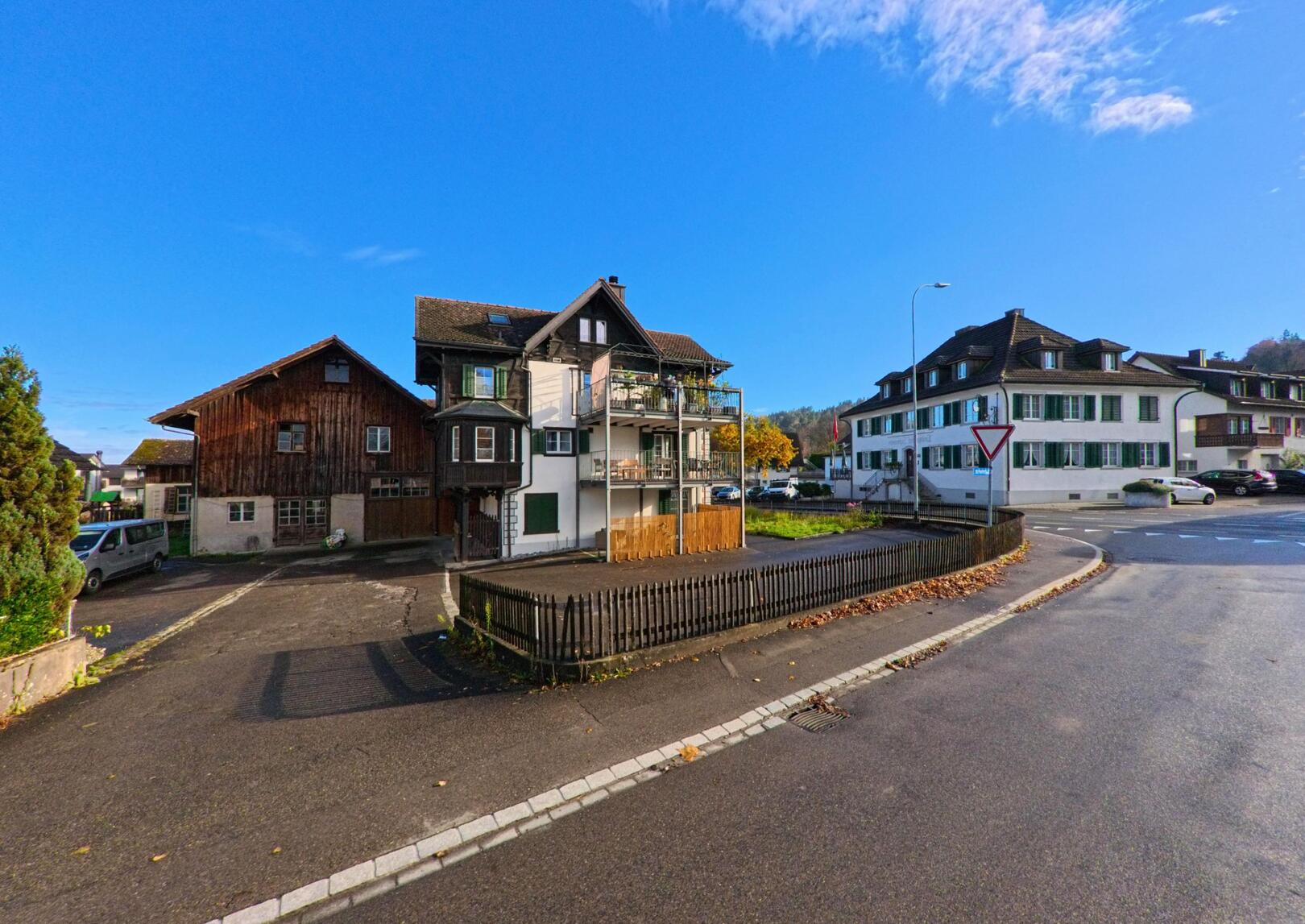 An einer Strassenkreuzung in Felben-Wellhausen (8552, Kanton Thurgau) stehen traditionelle Wohnhäuser neben einem Vortritts-schild bei klarem Himmel.