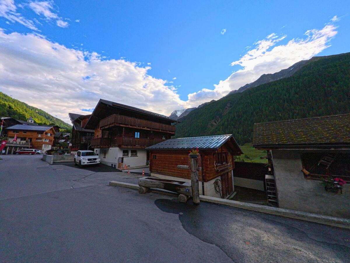 Zwischen traditionellen Holzhäusern in Ferden (3916, Kanton Wallis) öffnet sich der Blick auf die umliegenden Wälder und Berge im sonnigen Tal.