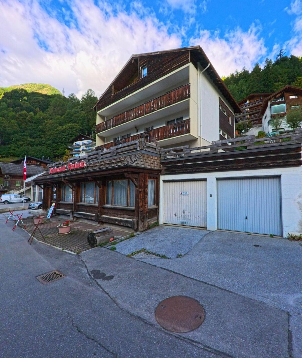 In Ferden (3916, Kanton Wallis) steht ein mehrstöckiges Wohnhaus mit Holzverkleidung und einem Restaurant im Erdgeschoss an einer ruhigen Strasse.