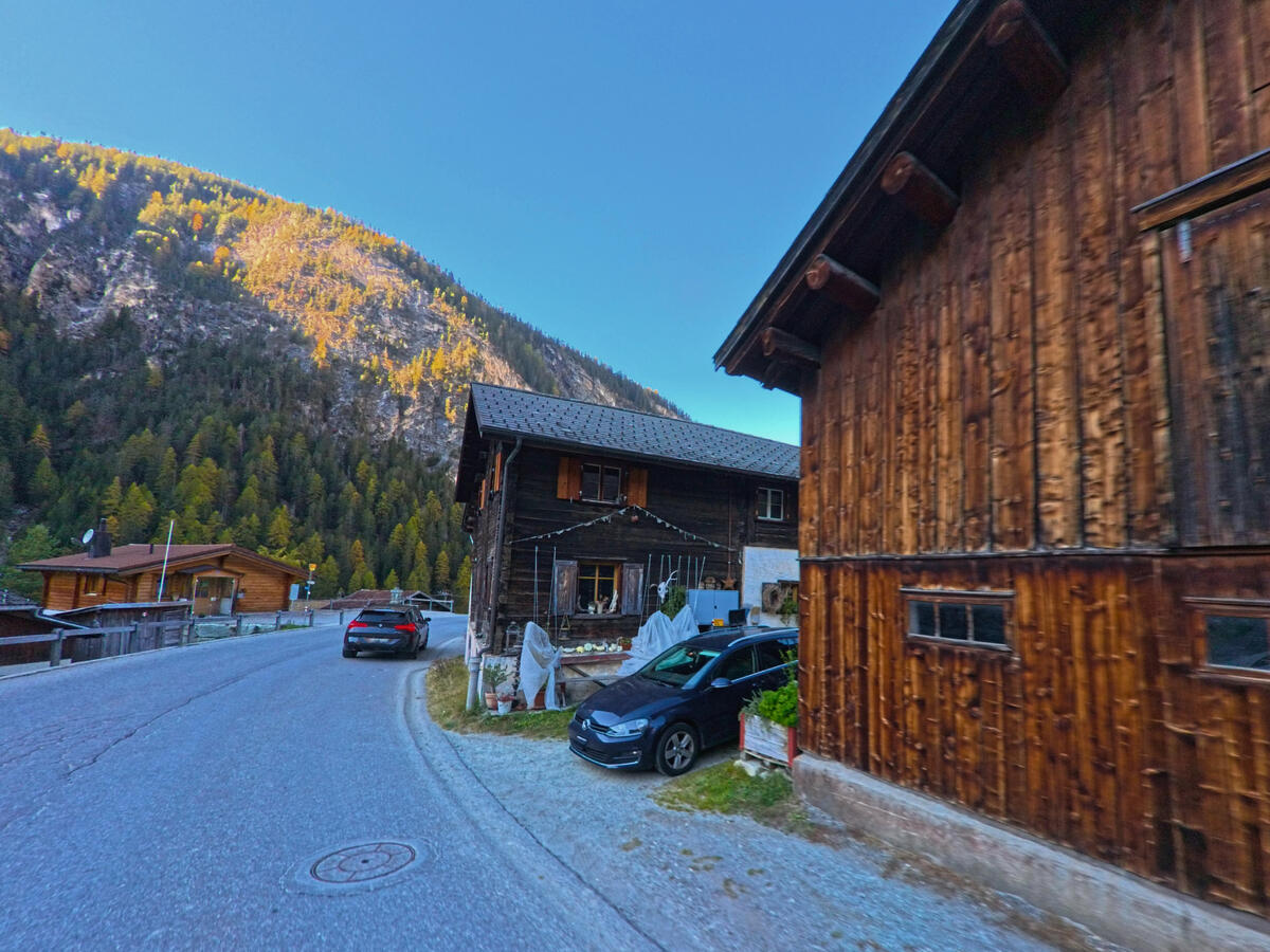 Holzgebaeude saeumen eine Kurve der Dorfstrasse in Ferrera (7444, Kanton Graubünden).