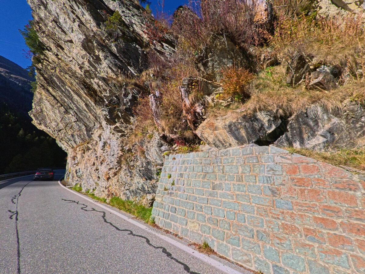 Entlang einer schmalen Strasse stuetzt eine gemauerte Wand den Fels in Ferrera (7444, Kanton Graubünden).