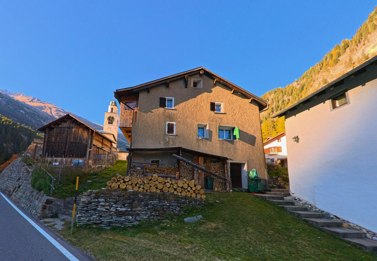 Ein Wohnhaus mit Natursteinsockel steht oberhalb einer Gruenflaeche in Ferrera (7444, Kanton Graubünden).